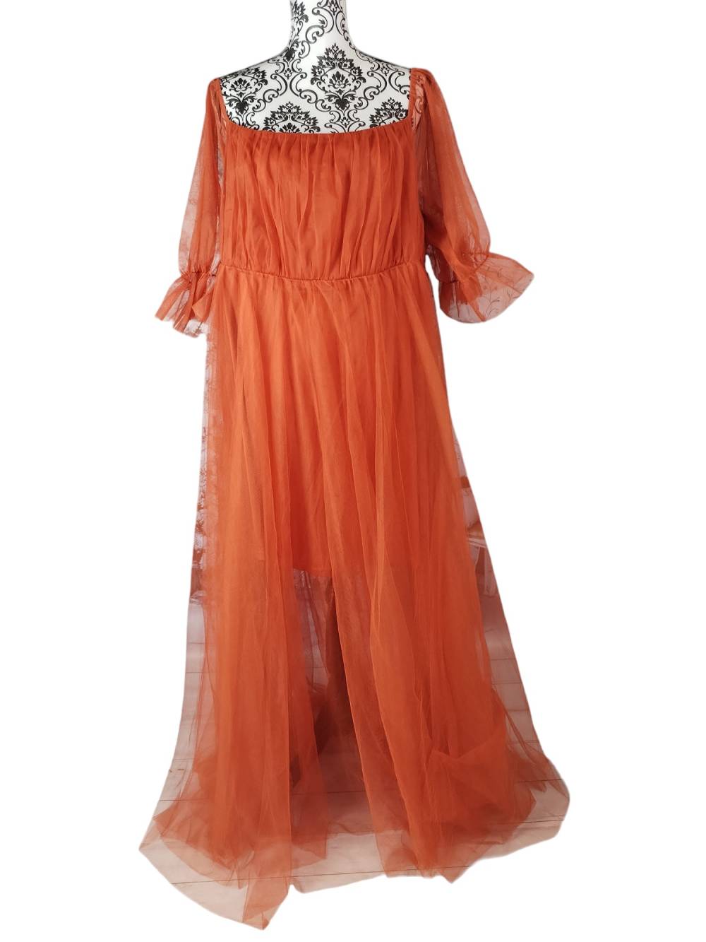 Robe orange brûlée .Cette robe de maternité présente une encolure carrée et des manches longues bouffantes, ainsi qu'une double jupe , la fermeture zip se fait au dos 